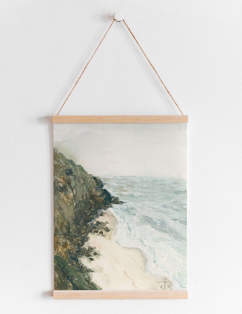 K&ouml;nnte beinhalten: Ein Aquarellbild einer felsigen Klippe, die auf einen Sandstrand mit t&uuml;rkisfarbenen Wellen blickt, die an der K&uuml;ste brechen. Das Bild hat eine ged&auml;mpfte Farbpalette mit Gr&uuml;nt&ouml;nen, Blau- und Wei&szlig;t&ouml;nen.