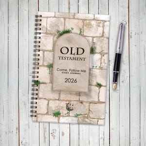 May include: A spiral-bound study journal with the text "OLD TESTAMENT" and "Come, Follow Me STUDY JOURNAL 2026" on the cover. The cover design features a stone wall and a tombstone-shaped graphic. A black and silver fountain pen rests beside the journal.