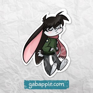 May include: A sticker of a cartoon bunny character with long black ears and a pink interior. The bunny is wearing a green jacket, a red scarf, and grey trousers. The sticker has the text "gabapple.com" at the bottom.