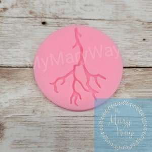 May include: Pink silicone mold with a raised design of a tree branch with many branches. The mold is on a wooden surface.