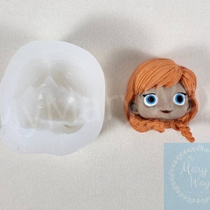 May include: A silicone mold for making a fondant or gumpaste figure of a girl with red hair and blue eyes. The mold is white and the figure is orange and brown.