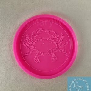 May include: Pink silicone mold with a raised design of a crab. The mold is round and has a raised edge.