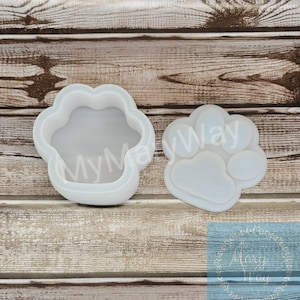 May include: Two white silicone molds shaped like a paw print. The mold on the left is a 3D paw print with a hollow center. The mold on the right is a flat paw print.