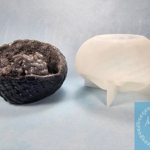 May include: Two resin molds. One is a dark gray, textured, half-sphere with a detailed interior. The other is a translucent white, rounded shape with a pedestal base. The molds are for mixed media art.
