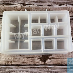 May include: A clear, rectangular silicone mold with multiple compartments of varying sizes. The mold is designed for crafting and features a series of square and rectangular spaces, ideal for creating small, organized items. The text "My Mary Way" is visible.