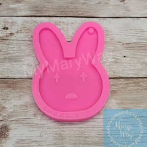 May include: Pink silicone mold shaped like a bunny rabbit with a small hole at the top. The bunny has two small crosses for eyes and a small curved line for a mouth.