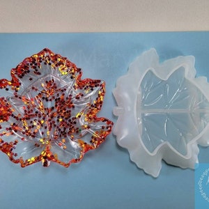 May include: A clear resin leaf tray with orange and red glitter embedded in the resin. The tray is shown next to a white silicone mold of a leaf.