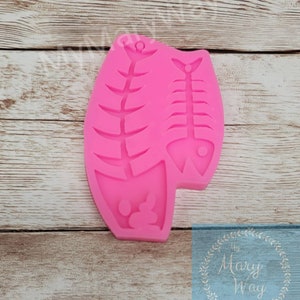 May include: Pink silicone mold with two fish bone shapes. The mold is designed to create resin or polymer clay charms.