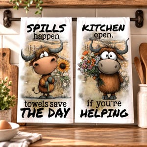 Peut inclure: Deux torchons de cuisine blancs suspendus à une barre. Le torchon de gauche présente une vache highland dessinée tenant un tournesol avec le texte "SPILLS happen towels save THE DAY". Celui de droite montre une vache avec des fleurs et "KITCHEN open, if you're HELPING".
