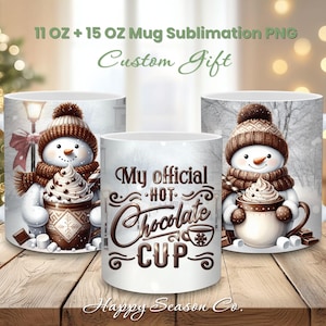 Könnte beinhalten: Weiße Keramikbecher mit Wintermotiven. Ein Becher zeigt einen Schneemann mit einer Tasse heißer Schokolade, ein anderer den Text "My official HOT Chocolate CUP". Die Becher sind 312 ml und 425 ml.