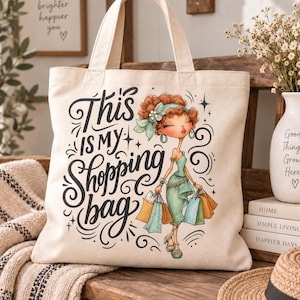 May include: A cream-colored canvas tote bag featuring the black text This is my Shopping bag and a colorful illustration of a person with curly brown hair wearing a green dress and holding multiple shopping bags in various colors.