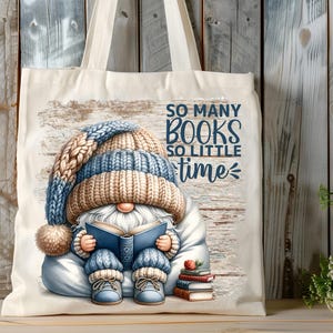 May include: A white canvas tote bag featuring a blue and brown gnome reading a book. The gnome is wearing a blue and brown knitted hat. The bag has the text "So many books so little time" printed on it.