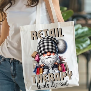 Puede incluir: Una bolsa de lona blanca con un gnomo de cuadros blanco y negro que lleva bolsas de la compra. El texto "Retail Therapy heals the soul" está impreso en la bolsa.