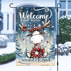 Może przedstawiać: Flaga ogrodowa o tematyce zimowej z kreskówkowym łosiem z wieńcem i porożem, na tle zaśnieżonego lasu. Flaga głosi "Welcome to our winter Wonderland" w fantazyjnej czcionce, z niebiesko-białą kolorystyką.