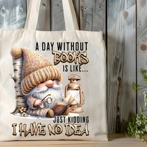 May include: A white tote bag featuring a gnome holding a book and a lantern. The bag has the text "A day without books is like... Just kidding I have no idea" printed on it.