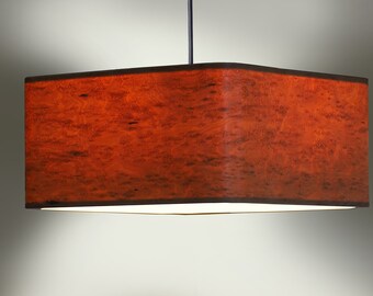 Könnte beinhalten: Rechteckige Pendelleuchte mit rotbraunem Schirm. Der Schirm hat eine strukturierte, holzähnliche Optik mit dunkelbraunem Rand. Das Licht hängt an einem schwarzen Kabel. Der untere Rand strahlt sanft.
