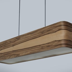 Könnte beinhalten: Eine rechteckige Pendelleuchte mit Holzfurnier. Die Leuchte hat eine hellfarbene Mittelplatte und ein dunkleres Holzmaserungsmuster an den Seiten. Sie hängt an zwei dünnen schwarzen Schnüren.