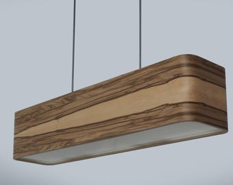 Könnte beinhalten: Eine rechteckige Pendelleuchte mit Holzfurnier. Die Leuchte hat eine hellfarbene Mittelplatte und ein dunkleres Holzmaserungsmuster an den Seiten. Sie hängt an zwei dünnen schwarzen Schnüren.