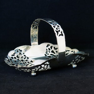 May include: A silver serving basket with a decorative handle and a scalloped edge. The basket has a delicate, openwork design and sits on three feet.