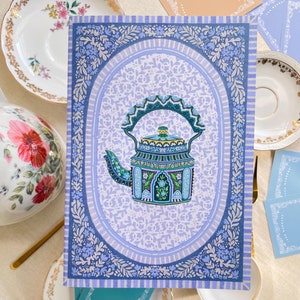 May include: A blue and white patterned card with a decorative teal teapot in the center. The teapot has a green and gold design and is surrounded by a floral border.