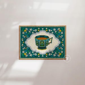 May include: A teal blue and gold teacup with a floral pattern sits in the centre of a square print with a teal blue and green floral border.