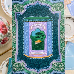 May include: A teal green and purple illustrated design of a tea tin with the text "Sree Mangal Finest Tea Merchants" and "Premium Blends" on it. The tin is surrounded by a decorative border with floral and leaf motifs.
