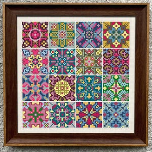 May include: A framed cross-stitch sampler featuring sixteen colorful geometric patterns. The patterns are arranged in a grid, with each square showcasing a unique design in shades of pink, blue, green, yellow, and purple. The frame is a dark brown color.
