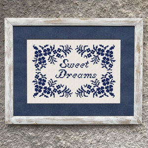 May include: A white framed picture with a blue mat and a white background with blue embroidery of flowers and the text "Sweet Dreams".