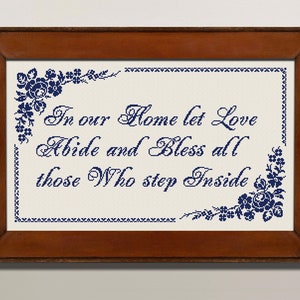 May include: A framed cross-stitch with a white background and blue embroidery. The embroidery reads "In our Home let Love Abide and Bless all those who step Inside".
