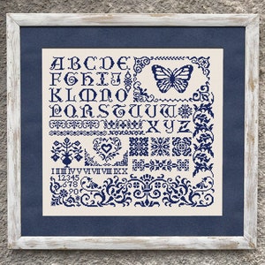 Puede incluir: Un sampler de punto de cruz enmarcado con fondo blanco y bordado azul. El sampler presenta el alfabeto, los números y un diseño de mariposa.