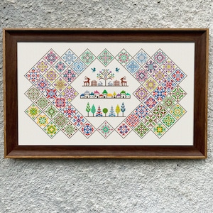 Puede incluir: Un diseño de bordado de punto de cruz colorido que presenta una escena de pueblo con casas, árboles y ciervos. El diseño está rodeado por un borde de cuadrados coloridos.