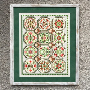 May include: A framed cross-stitch design featuring a repeating pattern of green, red, and brown geometric shapes. The design is set against a white background and framed with a white wood frame.
