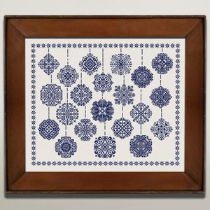 May include: A framed embroidery piece with a white background and a blue pattern of snowflakes hanging from a string. The snowflakes are arranged in a grid pattern.