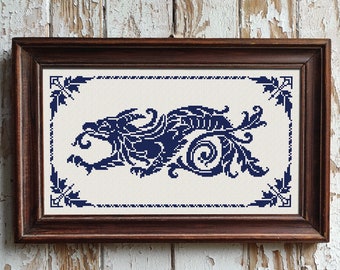 May include: A framed cross-stitch embroidery featuring a blue stylized dragon with intricate details. The dragon is surrounded by a decorative border of leaves and swirls.