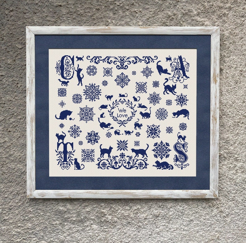 May include: A framed cross-stitch design featuring a blue and white pattern of cats, flowers, and the words "We Love Cats".
