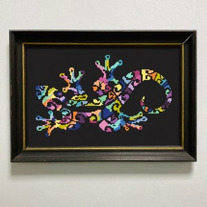 Könnte beinhalten: Ein gerahmtes Kreuzstich-Kunstwerk, das ein farbenfrohes Gecko auf schwarzem Hintergrund zeigt. Das Gecko besteht aus verschiedenen geometrischen Formen und Mustern in den Farben Rosa, Blau, Grün, Gelb und Orange.