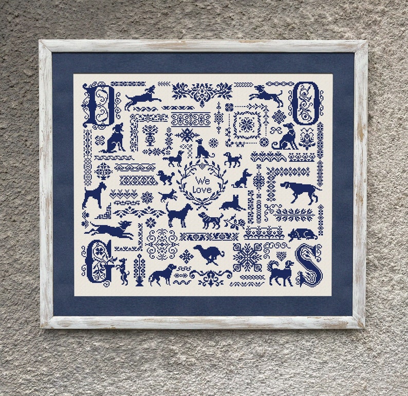 May include: Framed cross-stitch artwork featuring various dog silhouettes in navy blue on an off-white background. The design includes decorative borders, floral elements, and the text "We Love". The frame is white with a navy blue mat.