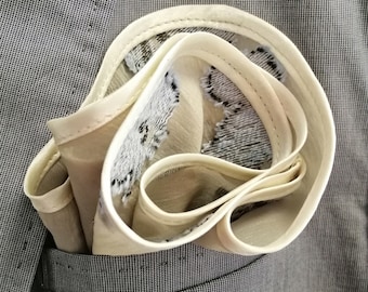 May include: A beige pocket square with a floral pattern, folded and placed in the pocket of a grey suit jacket.