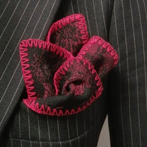 May include: A black pinstripe suit jacket with a pink patterned pocket square. The pocket square has a pink crocheted border.