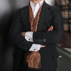 May include: A black pinstripe blazer with a brown patterned scarf and a white collared shirt. The blazer has a button closure and two pockets.