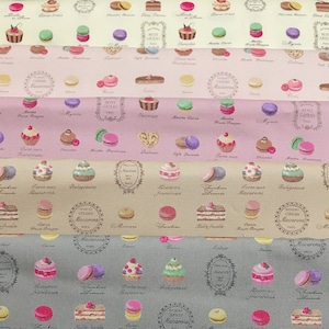 Op de afbeelding: Een roze en beige stof met een herhalend patroon van macarons, taarten en ander gebak. De stof heeft Frans-geïnspireerde tekst en illustraties.