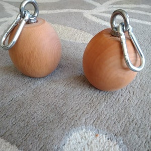 May include: Two wooden exercise balls with metal carabiners. The balls are brown and have a smooth surface. The carabiners are silver and have a loop on one end.
