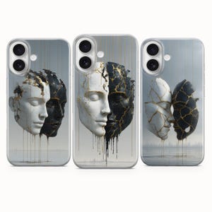 May include: Three phone cases with a surreal design. Each case features a split face, one half white, the other black, with gold accents. The background is a muted gray with a cityscape at the bottom.