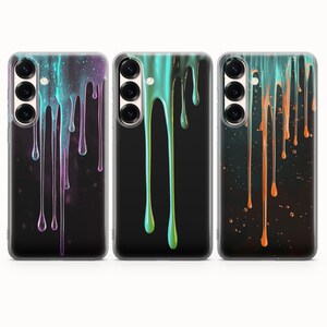 May include: Three clear smartphone cases featuring a liquid drip design. The first case has purple and teal drips, the second has bright green drips, and the third has orange drips. Each case displays a triple camera lens cutout on the upper left.