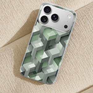 Può includere: Custodia trasparente per telefono con un design geometrico a cubo 3D nei toni del verde e del grigio. La custodia ha un bordo trasparente e copre il retro di uno smartphone con tre obiettivi.