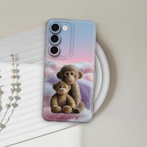 Könnte beinhalten: Handyhülle mit einem skurrilen Design mit einem Affen und einem Teddybären. Die Hülle hat einen Hintergrund mit Farbverlauf in Blau-, Rosa- und Lilatönen. Der Affe und der Teddybär sind braun und scheinen sich zu umarmen.