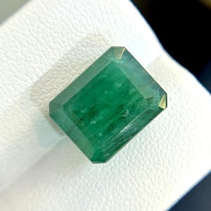 Puede incluir: Una gema de esmeralda verde vibrante tallada en forma de esmeralda. La gema tiene una forma rectangular con bordes biselados y una superficie lisa y pulida.