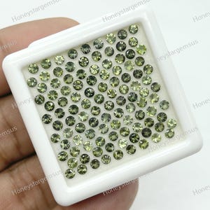 May include: A white tray filled with 100 round, green gemstones. The gemstones are arranged in a grid pattern.