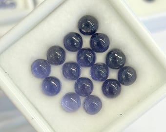 May include: A collection of round, polished gemstones in shades of deep blue and violet, arranged in a white tray. The gems have a smooth, reflective surface, and varying color intensities. The overall presentation suggests a focus on jewelry or gemstone materials.