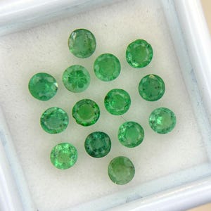 May include: A collection of round-cut emerald gemstones, each displaying a vibrant green hue. The gemstones are set against a white background, showcasing their clarity and brilliance. The emeralds are of varying sizes, creating a visually appealing arrangement.